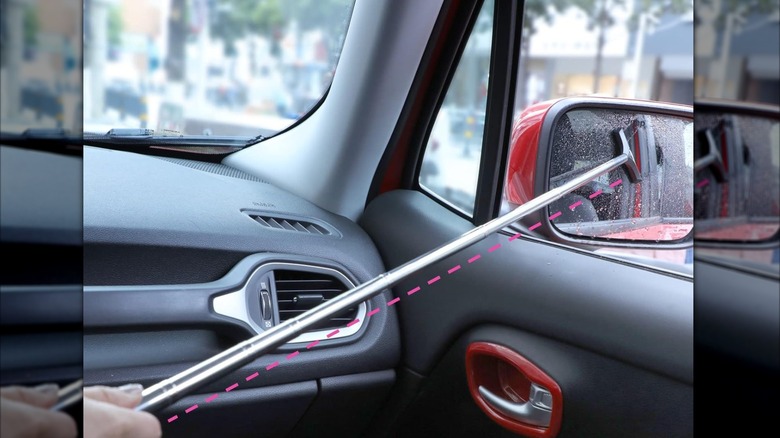 Hand using a squeegee on a pole to clean a car side mirror