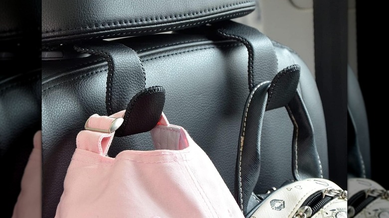 Two hooks attached to a car headrest holding a pink cap and a backpack