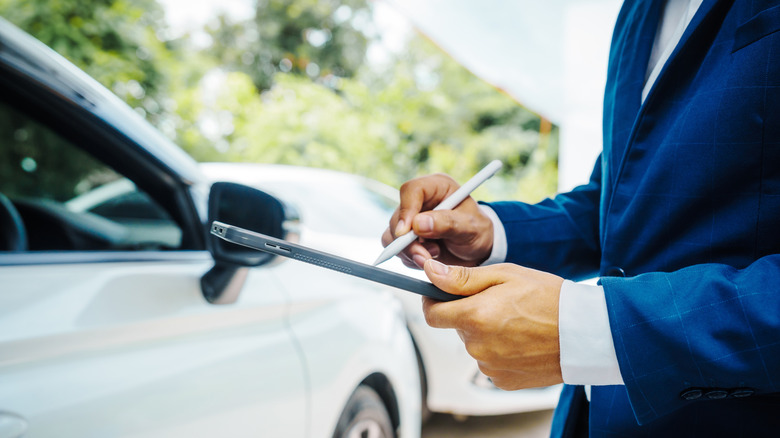 Man taking notes about white car on tablet
