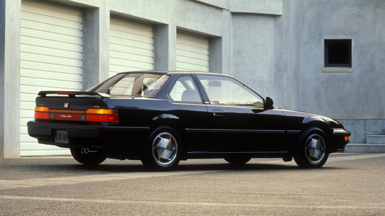 Rear three-quarter view of a black late-1980s Honda Prelude parked in front of a garage.