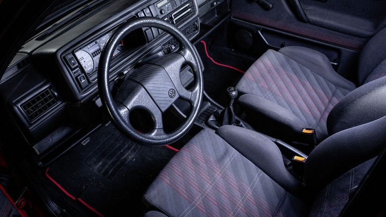 Interior view of a Mk2 Volkswagen GTI from the 1980s, featuring gray cloth sport seats with red plaid pattern.