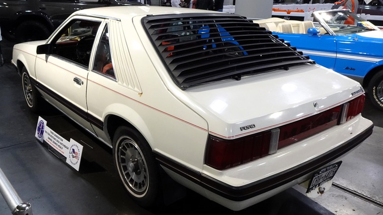 Rear-side view of a white third-generation Ford Mustang hatchback with black louvers.