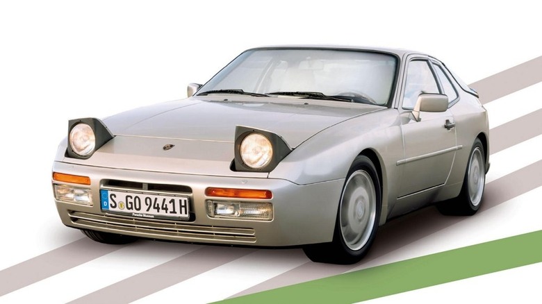 A silver Porsche 944 sports coupe with its pop-up headlights raised.