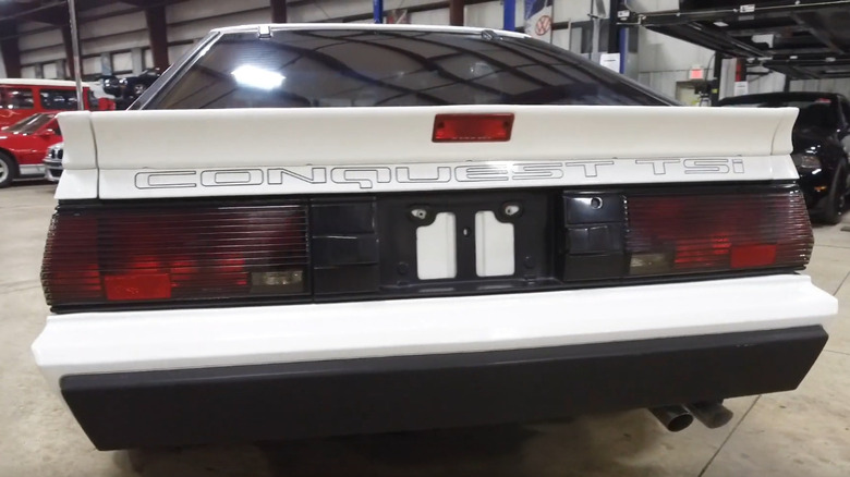 A rear view of a white 1987 Chrysler Conquest TSI sports coupe, showing its large silver "CONQUEST TSi" lettering across the hatch.