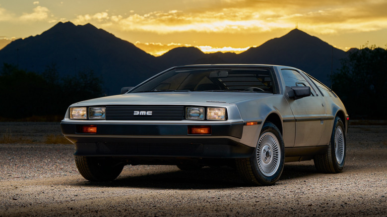 A DeLorean parked in front of a mountain range with the setting sun in the background