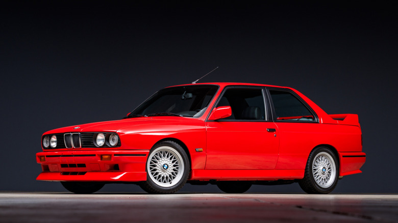 A red BMW E30 M3 parked on a black background