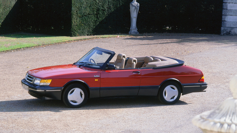 Red 1989 Saab 900 Turbo Convertible parked in the dirt driveway of a mansion