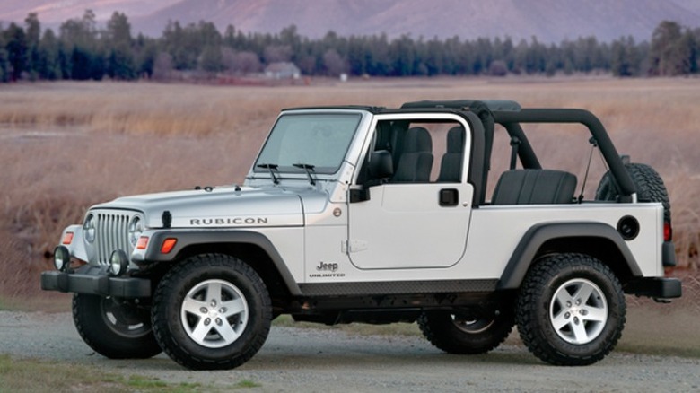 A silver Jeep Wrangler Rubicon Unlimited (TJ generation) with the top removed parked outdoors on a dirt path.