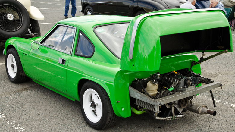 Green 1974 Ginetta 15 coupe seen from left rear with rear end folded up to reveal rear engine