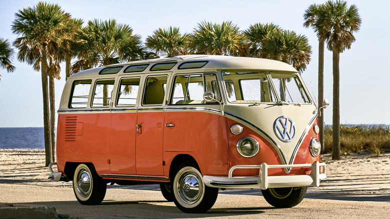 Orange and white Volkswagen Type 1 Bus seen from right front parked in front of palm trees at a beach
