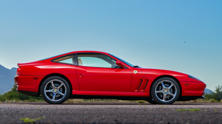 A side shot of a red Ferrari 550 Maranello on a road, parked.