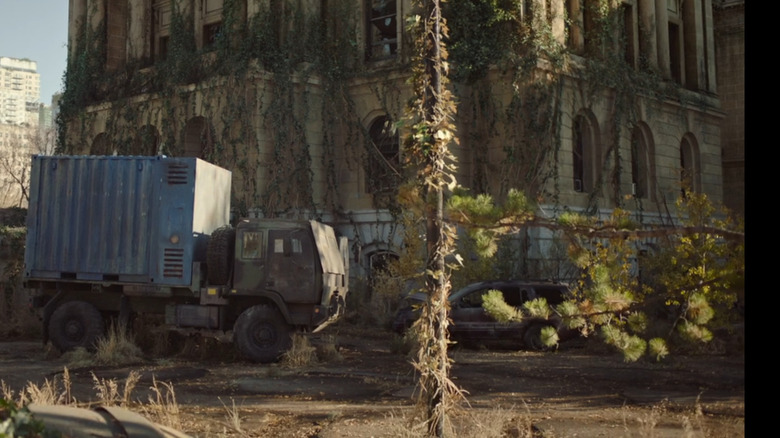 A military transport truck and a decaying Jeep Grand Cherokee sit abandoned outside an ivy-covered government building in "The Last of Us."