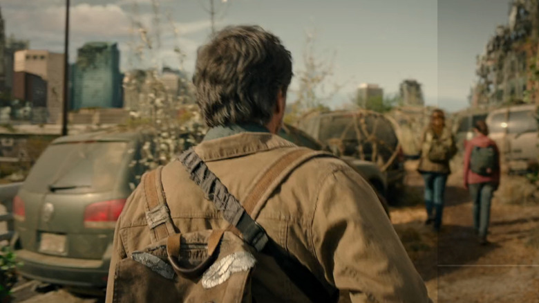 Joel follows Tess and Ellie past a Volkswagen Touareg and other abandoned cars as they navigate a crumbling cityscape in "The Last of Us."