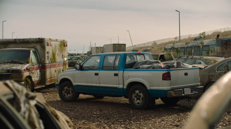 Bill's two-toned Chevy S-10 pickup truck from "The Last of Us" drives down a road partially blocked by abandoned vehicles.