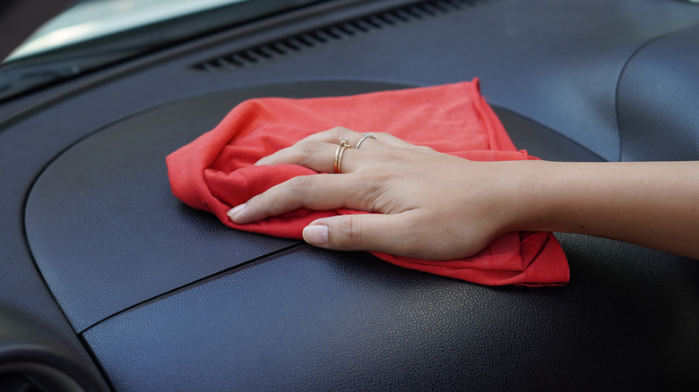 Hand using a red rag to wipe a car dashboard
