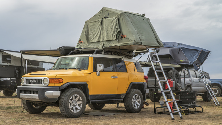 A Toyota FJ Cruiser complete with overland build, with its rooftop tent unfolded with a ladder visible