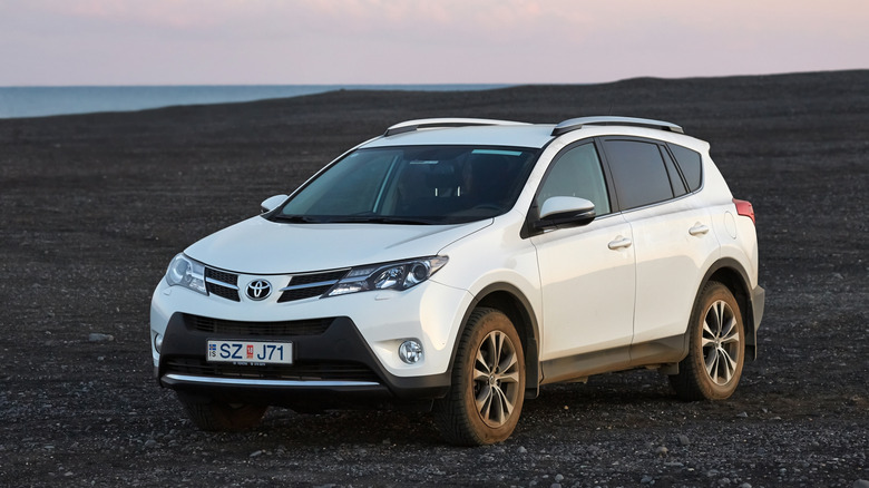A white 2015 pre-facelift Toyota RAV4 in an offroad setting against the dusky sky