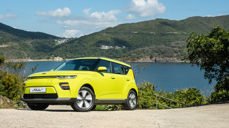 A lime green 2020 Kia Soul mini-SUV in front of a lake setting, parked at the side of a road