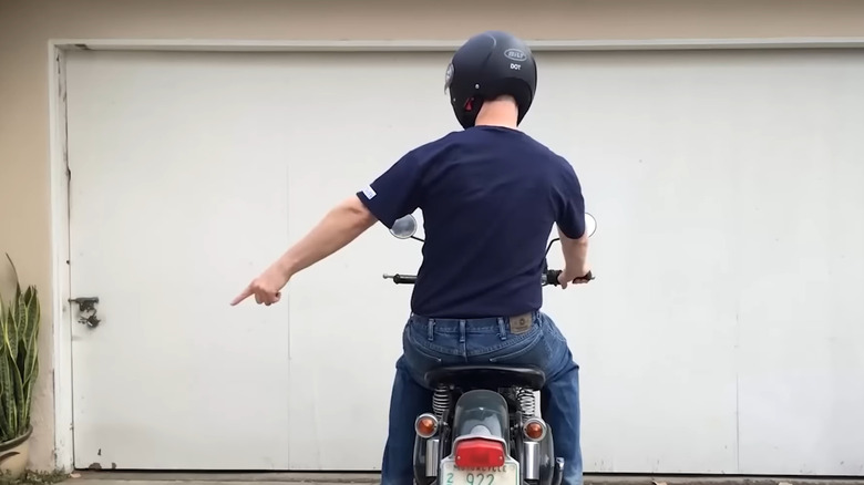A biker in a helmet  pointing to the left on a parked bike