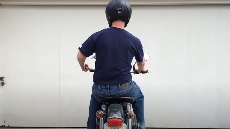 A rider in a blue t shirt and helmet showing the need fuel bike hand signal