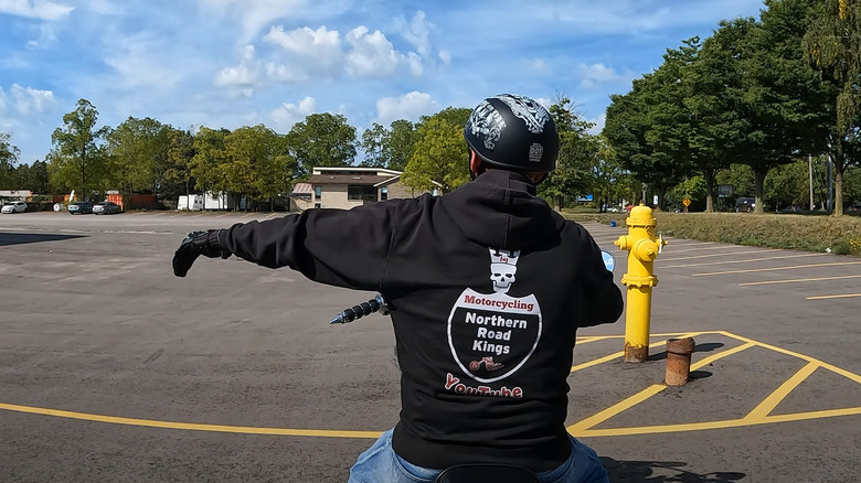 A biker wearing his club jacket demonstrating the slow down hand gesture