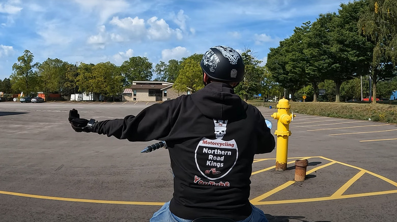 A biker wearing his club jacket demonstrating the speed up hand gesture