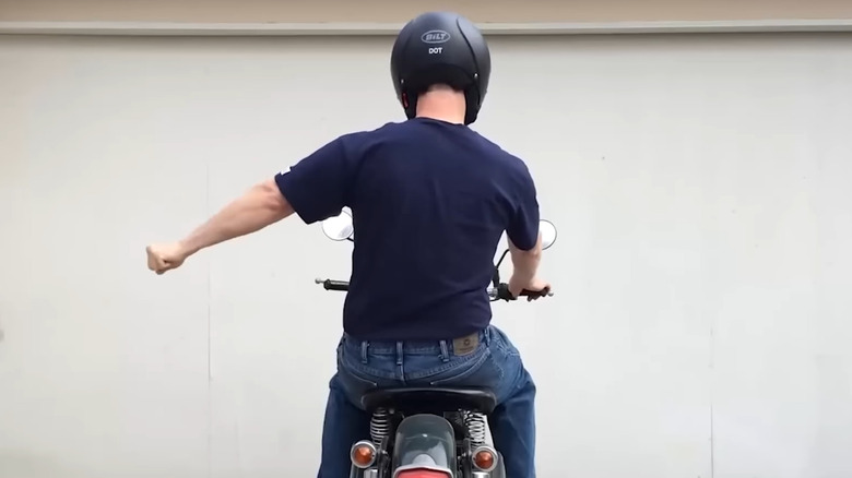 A rider in a helmet and Tee shirt displaying the stop for comfort motorcycle hand signal