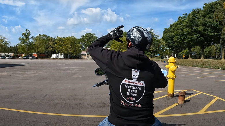 A parked biker showing viewers a hand signal against a clear blue sky.