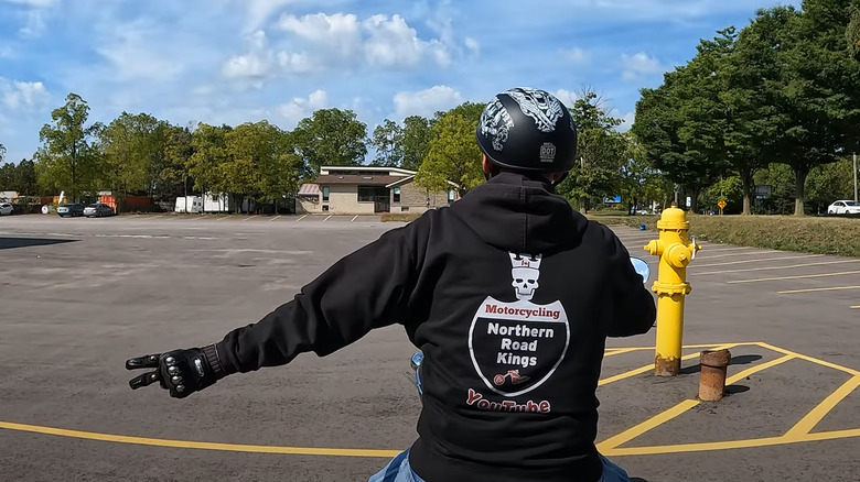 A biker in a jacket and helmet doing the biker wave hand gesture