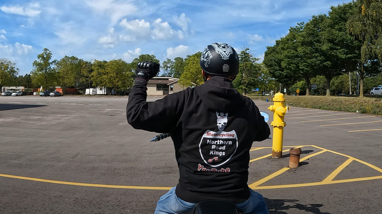 A biker wearing his club jacket demonstrating the turn right hand gesture
