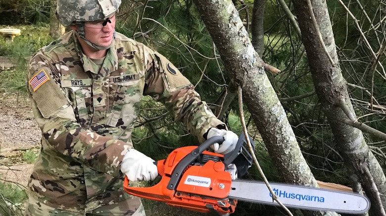 National Guard fella wielding a chainsaw against a tree