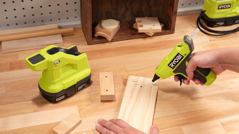 person using green glue gun on lumber
