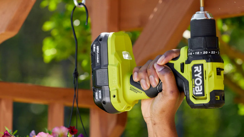 person using green drill near flowers