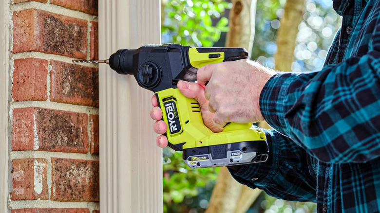 person using green rotary hammer on brick