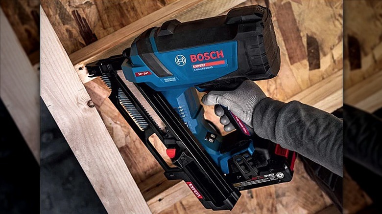 Using a framing nailer on an overhead wooden panel.