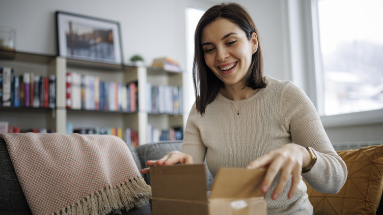 smiling woman opening package on the couch