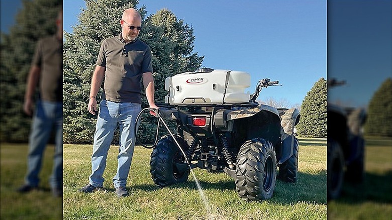 Man using a spot sprayer loaded onto an ATV to water the lawn.