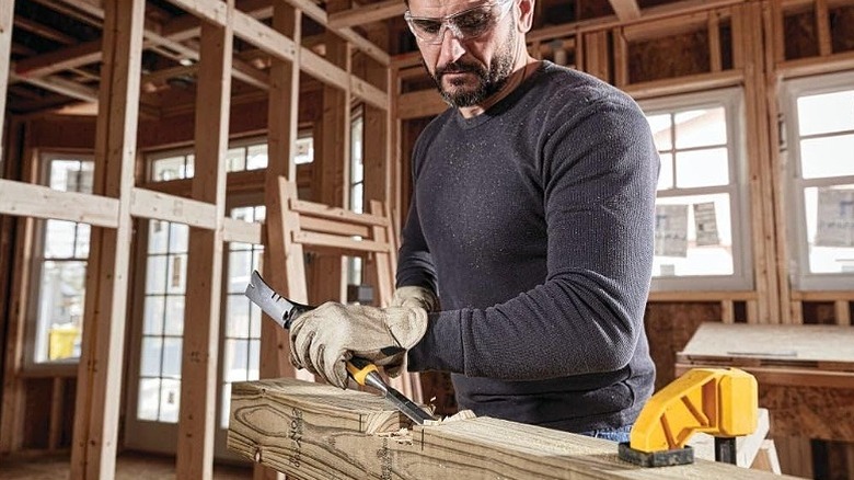 Man using wood chisel on a piece of wood in a workshop.