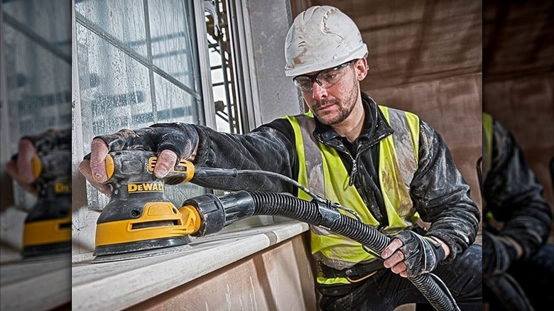 Construction worker using an orbit sander on a surface.