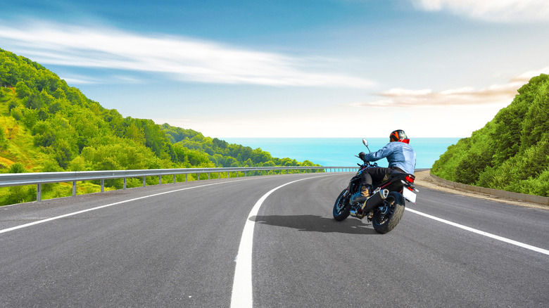 Person riding motorcycle along highway hillside