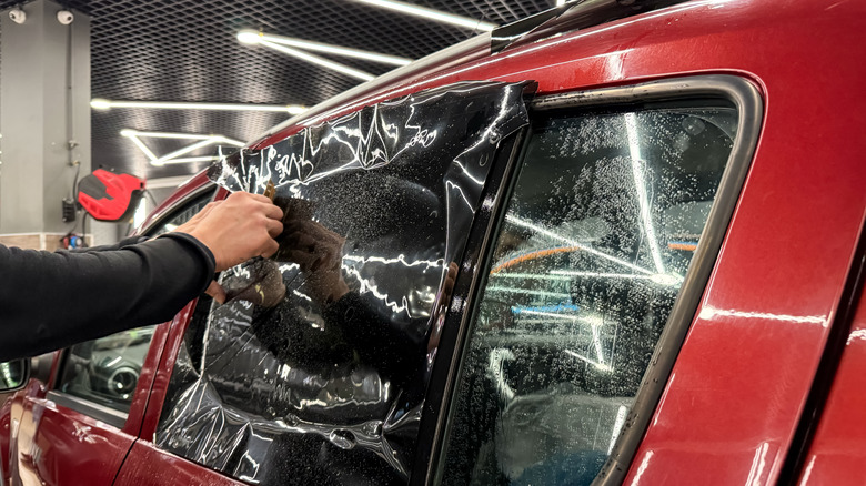 A male service tech installing a widow tint on a red car inside a detailing studio