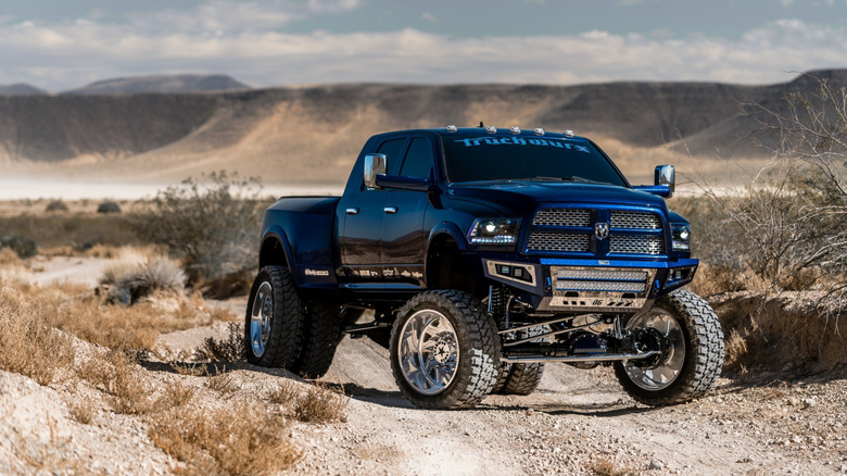 A lifted RAM 3500 pickup truck off-roading along a dusty road