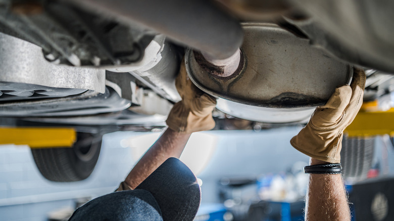 A mechanic inspecting the cat converter on the underneath of a vehicle