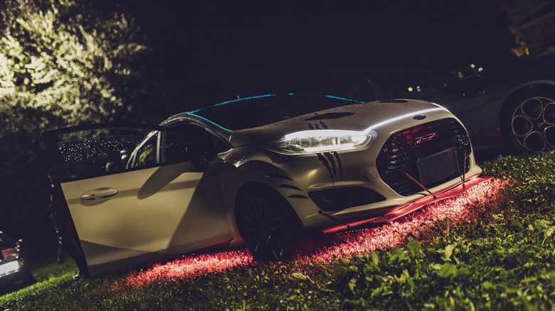 A grey ford fiesta parked on a lawn that is showing red underglow