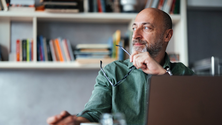 man with a beard thinking while using his laptop