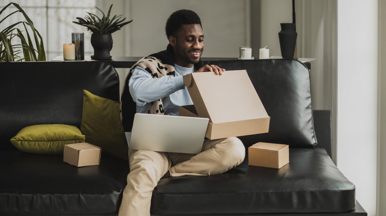 man sitting on a couch opening boxes