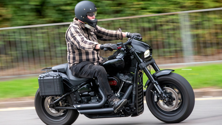 A rider in gear riding a Harley Fat Bob bike down a wooded British Road in 2018.