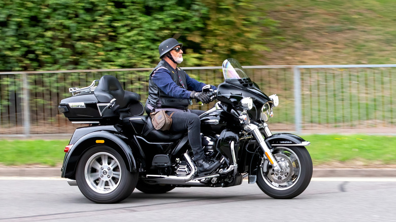 A rider wearing a helmet while riding a Harley-Davidson Tri-Glide motorbike finished in black down a road.