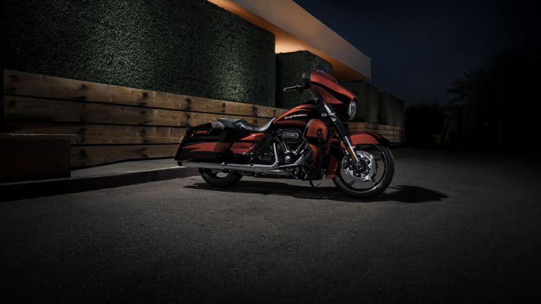 An orange CVO Street Glide parked next to a brutalist building at night