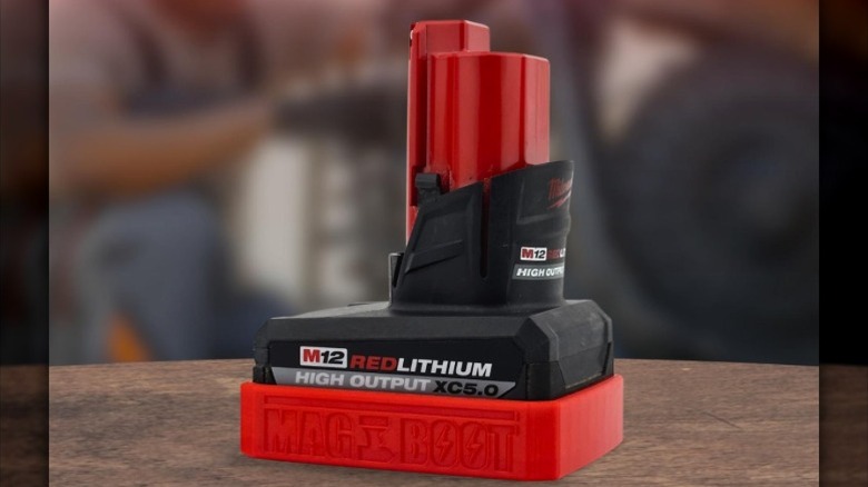 A Milwaukee M12 High Output XC5.0 battery with a red MAG-BOOT magnetic cover.